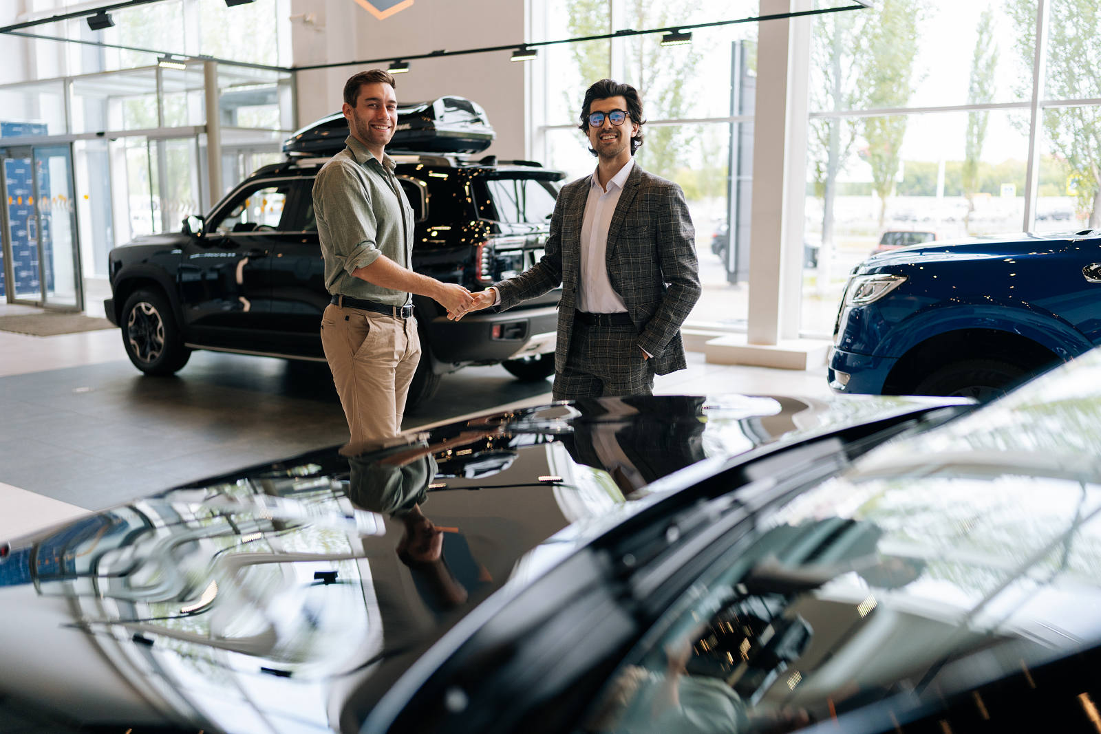 Händler und Kunde geben sich im Autohaus die Hand