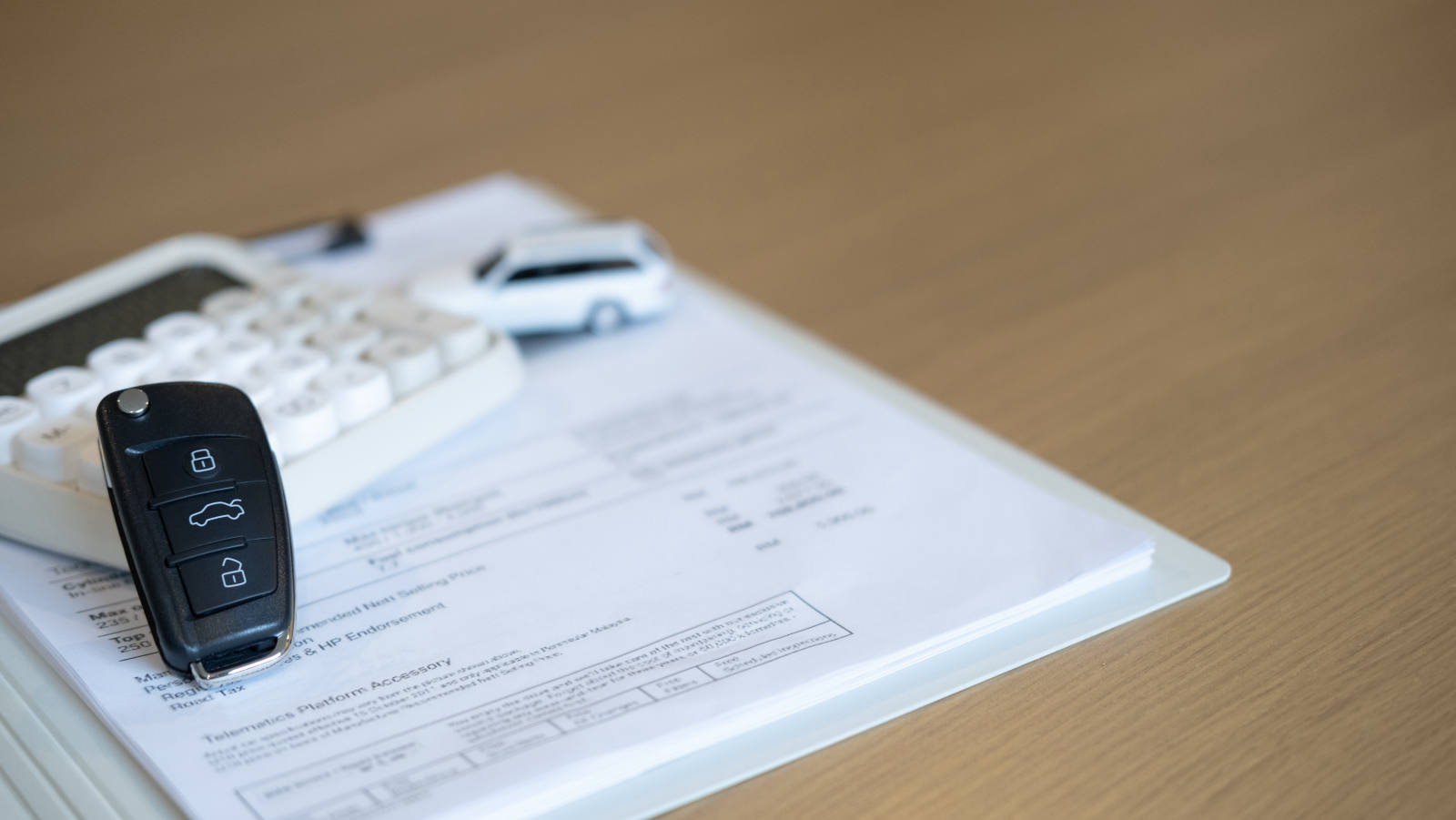 Autoschlüssel, Taschenrechner und Vertragsunterlagen auf einem Schreibtisch