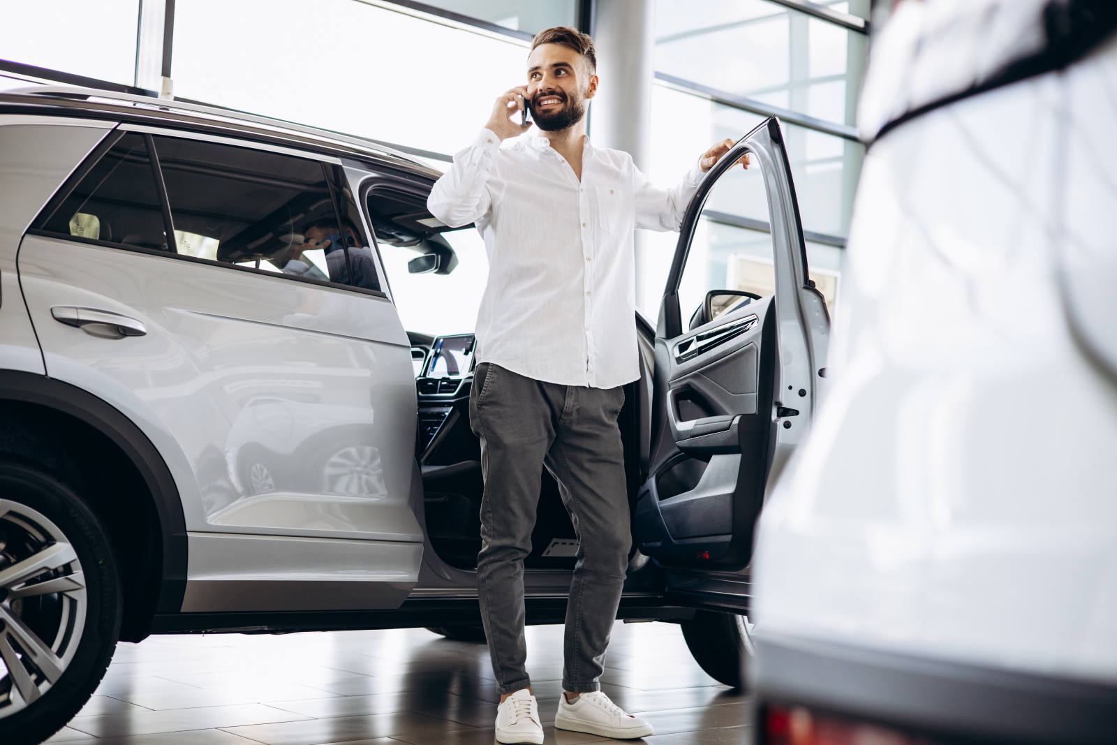 Mann telefoniert im Autohaus neben einem weißen Fahrzeug