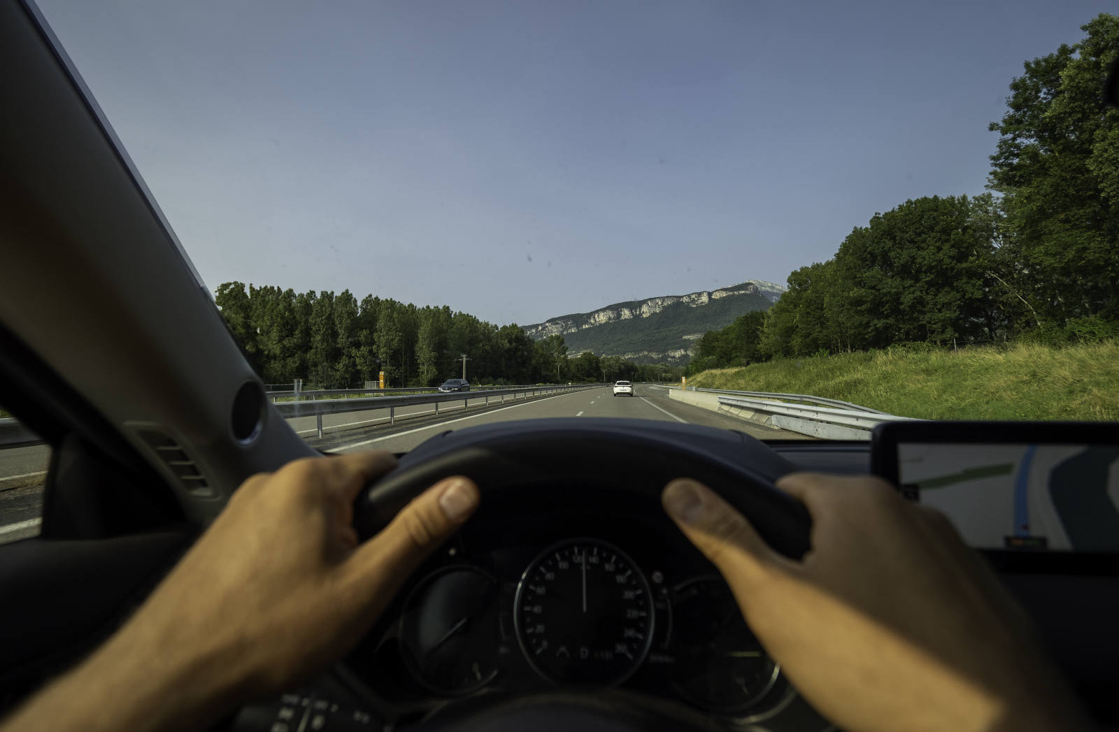 Hände am Lenkrad bei einer Fahrt auf der Landstraße mit Bergpanorama