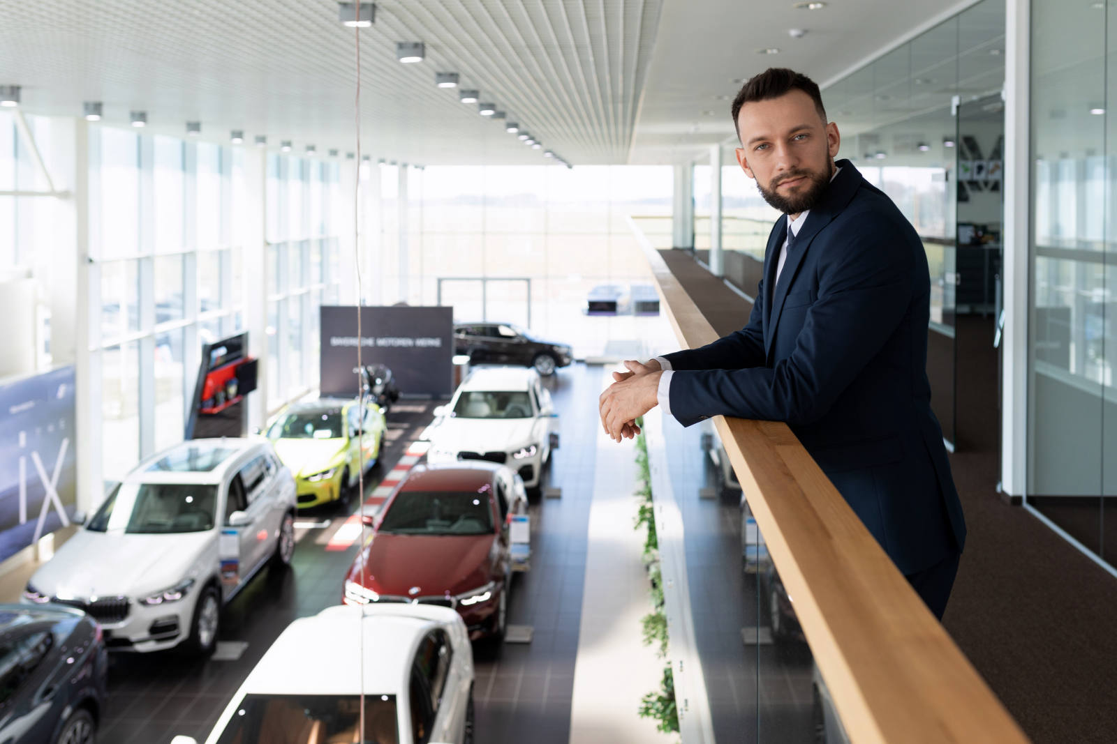 Geschäftsmann im Anzug blickt von einer Galerie auf einen Autohaus-Showroom